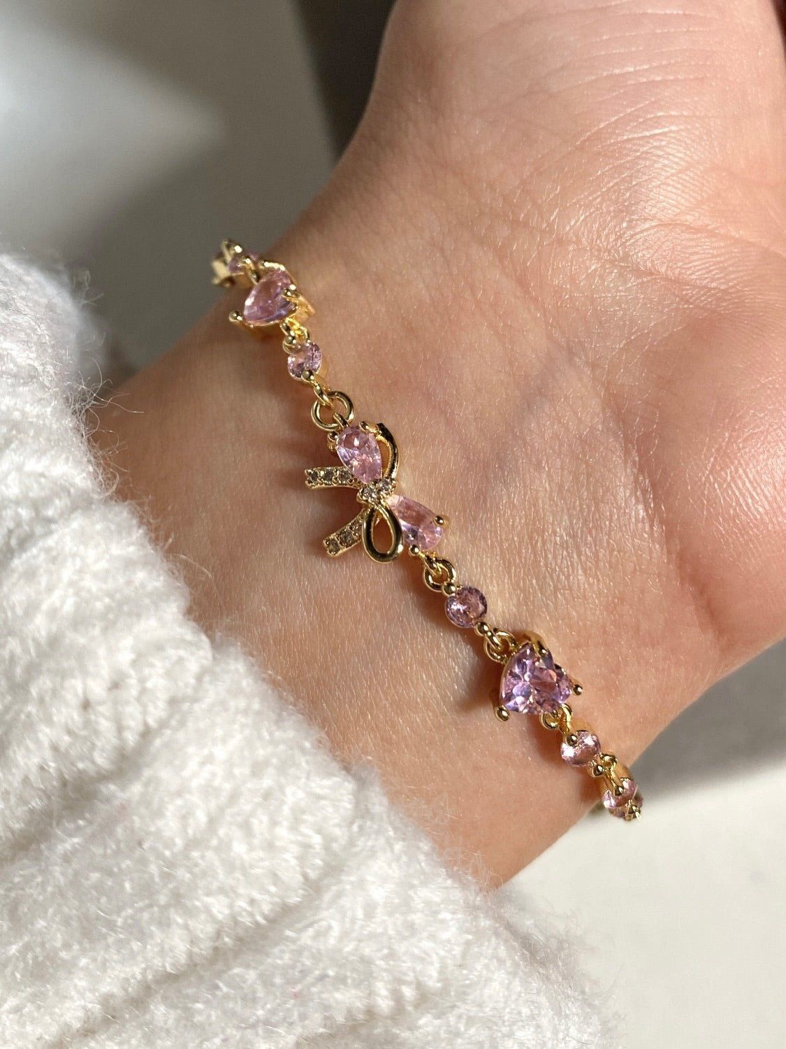 Close-up of the gold Bow Bracelet worn on the wrist, showing the pink stone bow charm