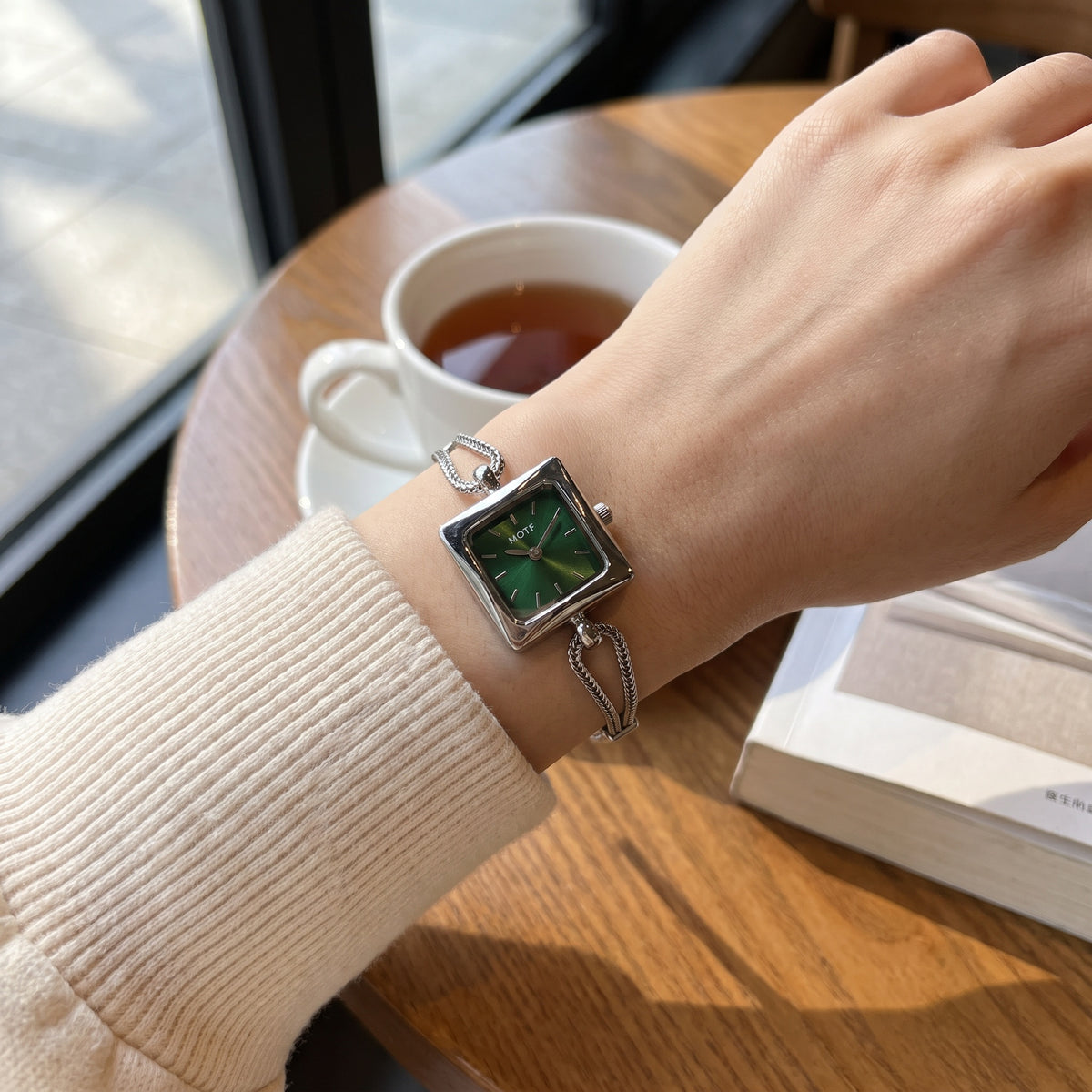 FairyLiora Queen's Watch in green, worn on the wrist at a cafe table